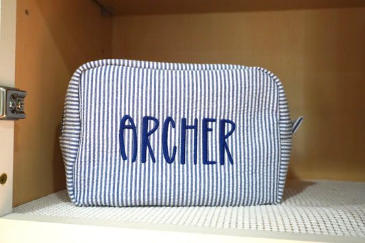 Blue and white striped pouch with 'ARCHER' text on a shelf